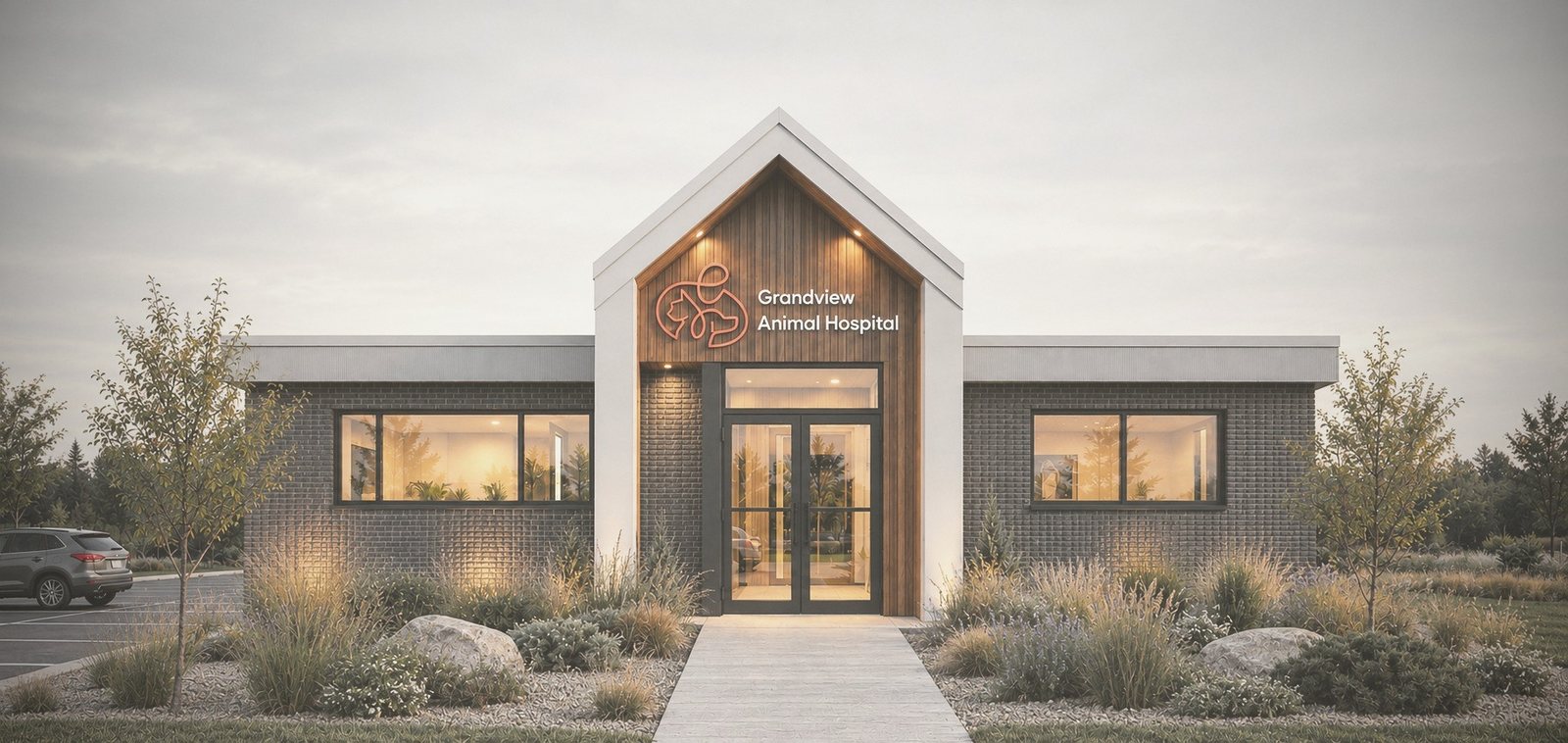 Animal hospital with a white gabled entry, vertical timber cladding and dark brick wings, lit warmly at dusk behind a planted meadow garden